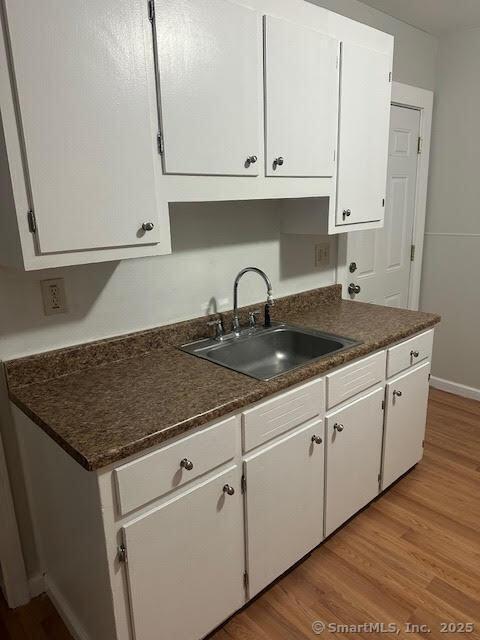 40 Orchard St, Bristol, CT 06010 - kitchen featuring a sink, white cabinets, light wood-type flooring, and dark countertops