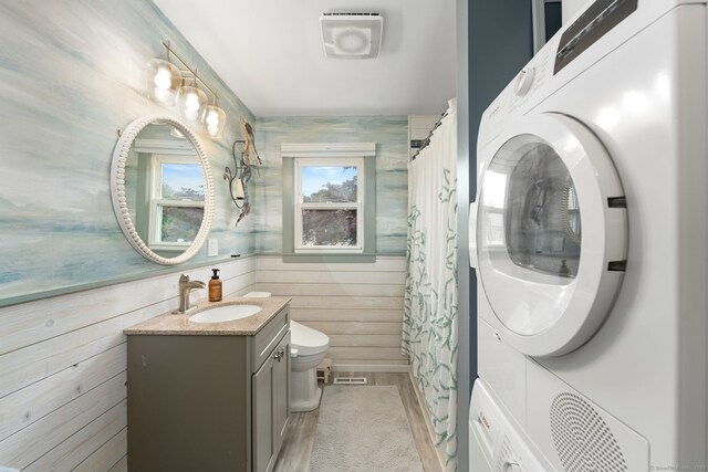 6 Meadow Dr, Waterford, CT 06385 - bathroom featuring vanity, toilet, stacked washer and clothes dryer, and wooden walls