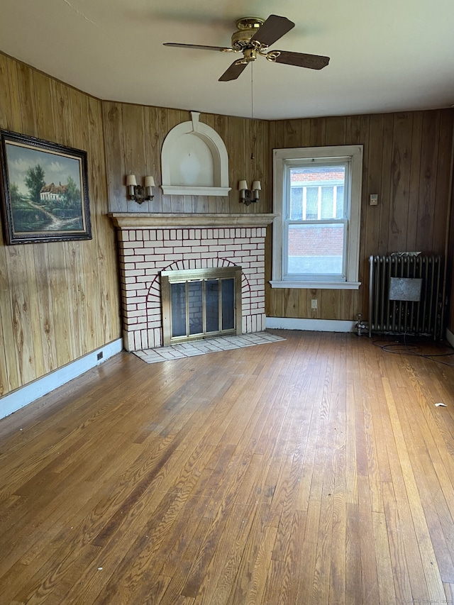 624 S Main St, Torrington, CT 06790 - unfurnished living room featuring radiator, a brick fireplace, wood finished floors, a ceiling fan, and wood walls