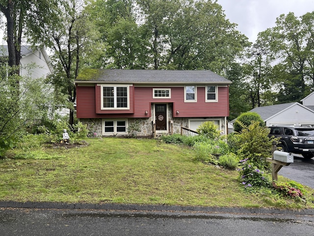 raised ranch with a garage, stone siding, and a front lawn