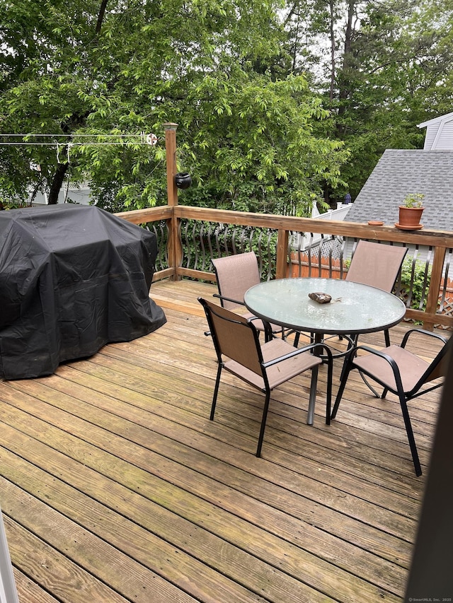 wooden deck featuring outdoor dining area, view of scattered trees, and a grill