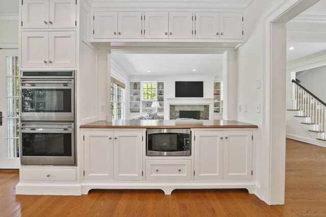 42 Morningside Dr S, Westport, CT 06880 - kitchen featuring appliances with stainless steel finishes, wood finished floors, white cabinets, a fireplace, and crown molding