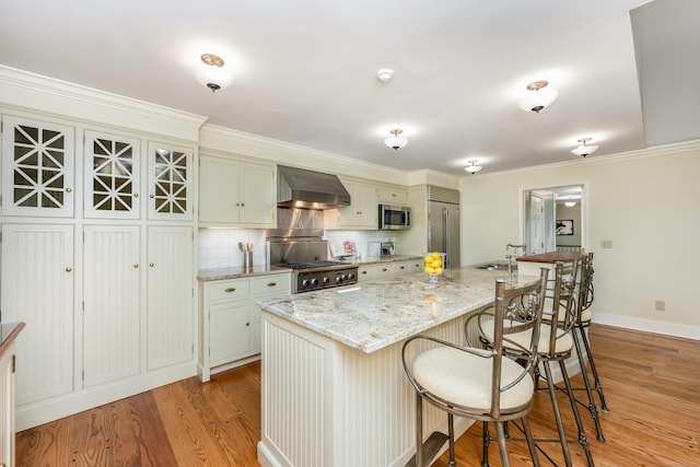 1208 Smith Ridge Rd, New Canaan, CT 06840 - kitchen featuring wall chimney exhaust hood, stainless steel appliances, light wood-type flooring, a breakfast bar, and an island with sink