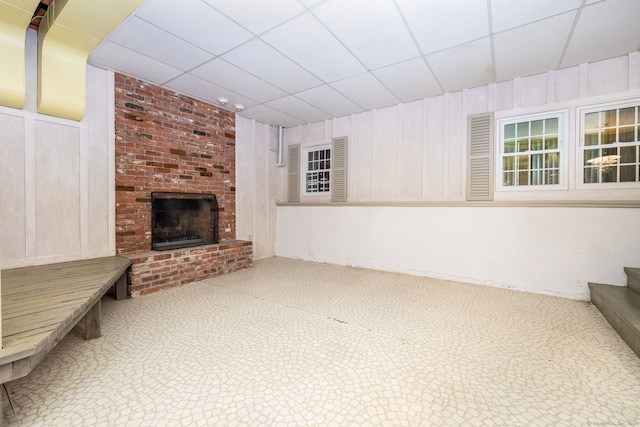 39 Chestnut Hill Rd, Simsbury, CT 06092 - unfurnished living room featuring carpet floors, a brick fireplace, wooden walls, stairway, and a drop ceiling