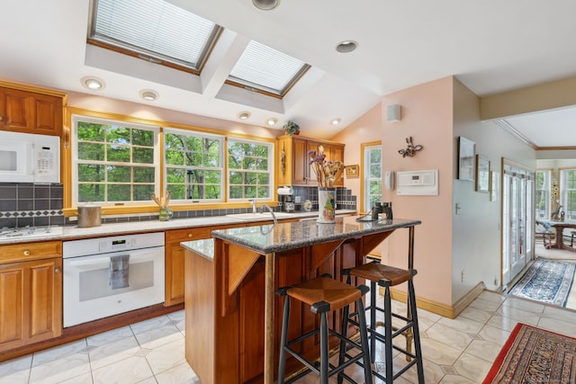 143 Petticoat Ln, East Haddam, CT 06423 - kitchen with white appliances, backsplash, a kitchen bar, a skylight, and brown cabinetry