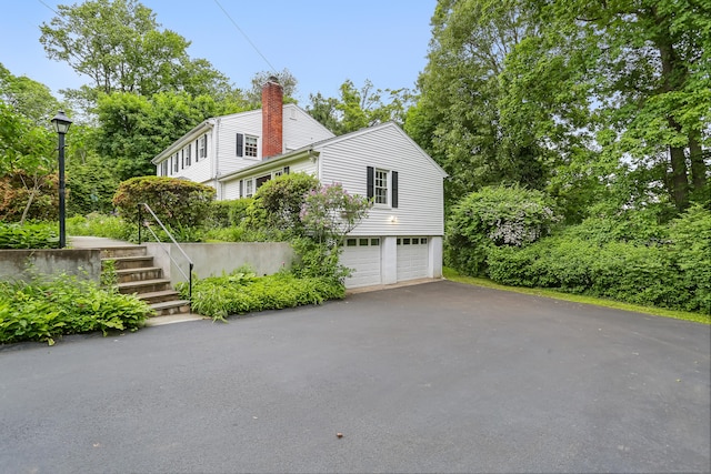 10 Crossland Pl, Norwalk, CT 06851 - view of home's exterior featuring a garage, asphalt driveway, stairway, and a chimney