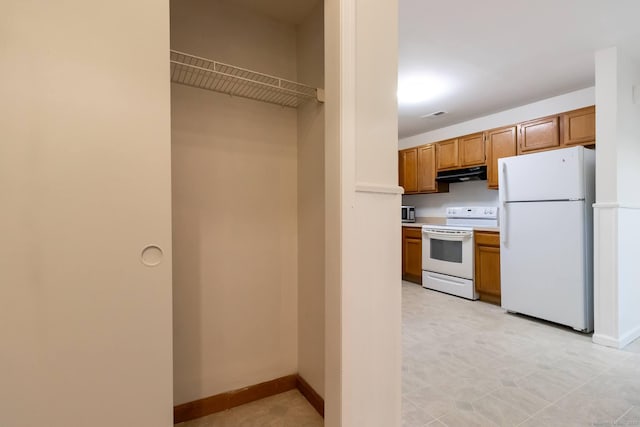 146 Macarthur Dr Unit 2B, Waterbury, CT 06704 - kitchen with white appliances, under cabinet range hood, light countertops, brown cabinetry, and baseboards