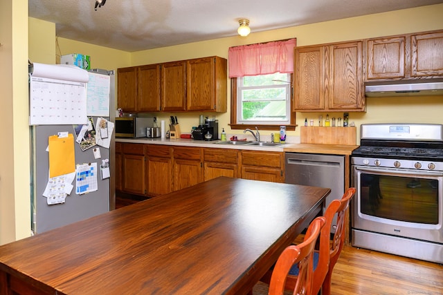 138 Baltic Hanover Rd, Sprague, CT 06330 - kitchen featuring appliances with stainless steel finishes, under cabinet range hood, a sink, brown cabinets, and light wood finished floors