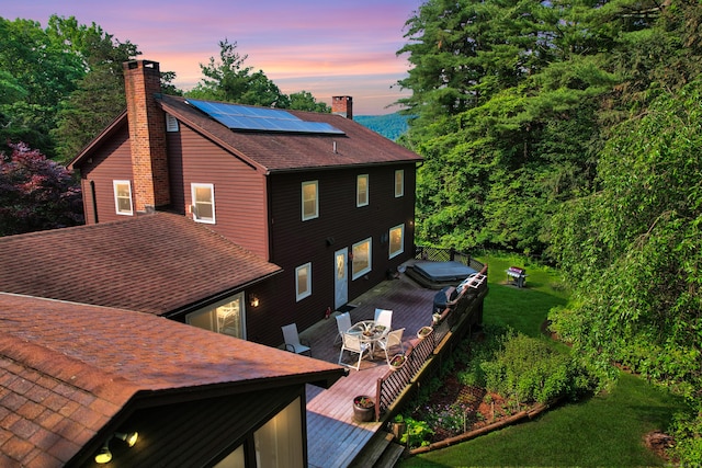 11 College Hill Rd, North Canaan, CT 06018 - back of property at dusk featuring outdoor dining space, a chimney, roof mounted solar panels, and a wooden deck