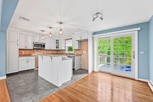 99 Redwood Dr, Bristol, CT 06010 - kitchen featuring stainless steel microwave, decorative backsplash, white cabinets, a breakfast bar area, and a kitchen island