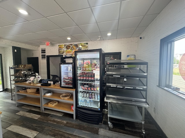 misc room with a drop ceiling, hardwood / wood-style floors, brick wall, beverage cooler, and recessed lighting
