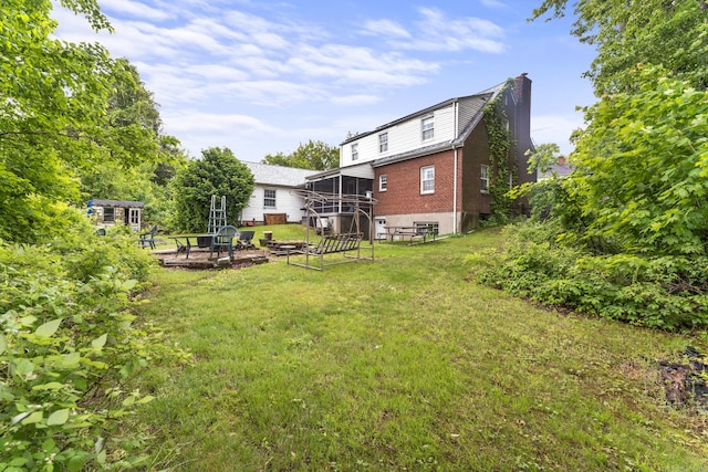 116 Maple St, Wethersfield, CT 06109 - rear view of property featuring a sunroom, an outdoor fire pit, a chimney, a yard, and brick siding