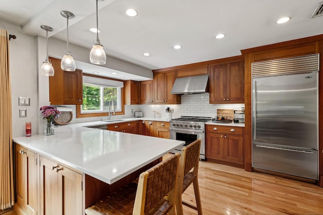 19 Huckleberry Dr S, Norwalk, CT 06850 - kitchen featuring high end appliances, wall chimney exhaust hood, a sink, a peninsula, and light countertops