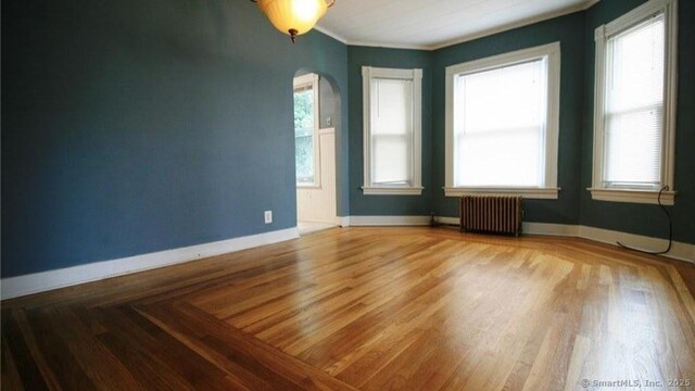 48 Moore Ave, New London, CT 06320 - empty room with radiator heating unit, arched walkways, healthy amount of natural light, wood finished floors, and crown molding