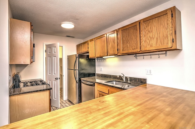107 Ferry Ct Unit 107, Stratford, CT 06615 - kitchen with appliances with stainless steel finishes, a sink, brown cabinetry, a textured ceiling, and dark stone countertops