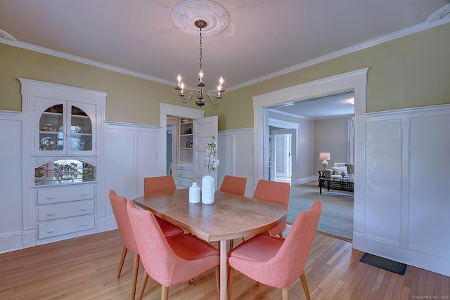 59 Golf St, Newington, CT 06111 - dining space featuring a chandelier, a decorative wall, light wood-type flooring, ornamental molding, and wainscoting