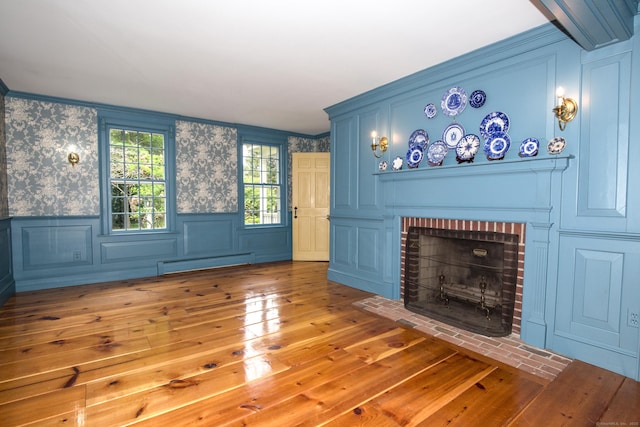 440 Mapleton Ave, Suffield, CT 06078 - unfurnished living room featuring a baseboard radiator, hardwood / wood-style floors, a decorative wall, a brick fireplace, and wainscoting