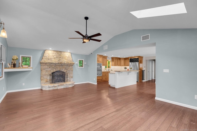 1190 Peck Ln, Cheshire, CT 06410 - unfurnished living room with a ceiling fan, vaulted ceiling, a stone fireplace, wood finished floors, and a skylight