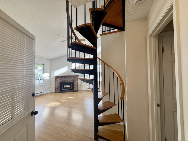 102 Beard Dr Unit 102, New Milford, CT 06776 - stairway featuring baseboard heating, a textured ceiling, wood finished floors, a brick fireplace, and baseboards