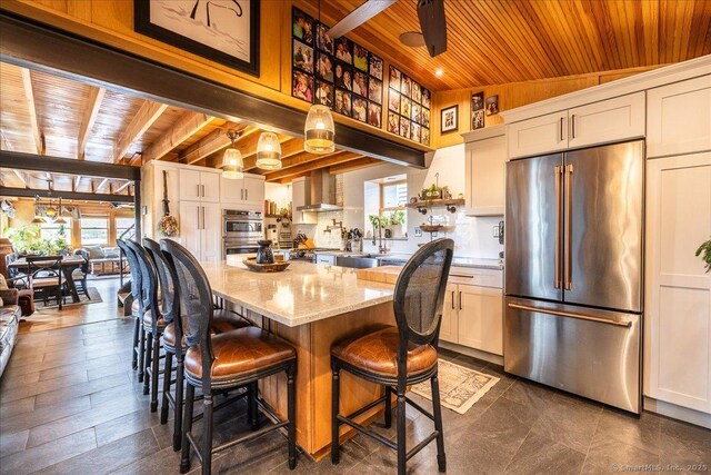 311 Captain Thomas Blvd, West Haven, CT 06516 - kitchen with stainless steel appliances, wood ceiling with exposed beams, wall chimney range hood, light stone countertops, and a sink