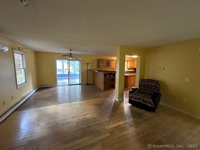149 Mill Hill Rd, Colchester, CT 06415 - unfurnished living room with dark wood-style flooring, a baseboard heating unit, a ceiling fan, and baseboards
