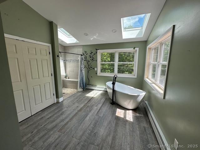 149 Mill Hill Rd, Colchester, CT 06415 - bathroom featuring a skylight, a soaking tub, a baseboard heating unit, a tile shower, and wood finished floors