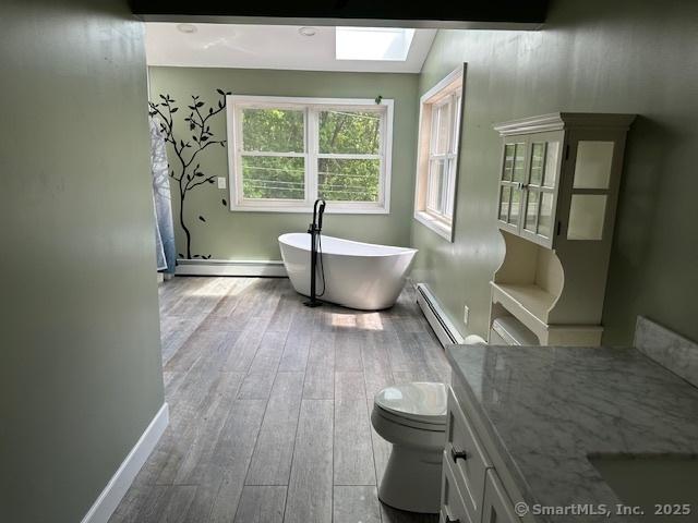 149 Mill Hill Rd, Colchester, CT 06415 - full bath with a baseboard heating unit, a freestanding tub, a baseboard radiator, wood finished floors, and toilet