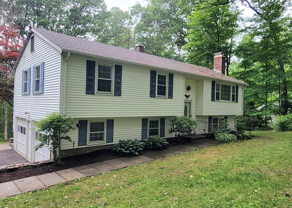 550 W Lake Ave, Guilford, CT 06437 - split foyer home featuring a chimney, a front lawn, an attached garage, and driveway