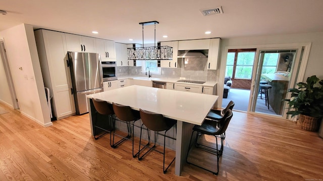 550 W Lake Ave, Guilford, CT 06437 - kitchen featuring stainless steel appliances, under cabinet range hood, a sink, a kitchen bar, and light wood finished floors