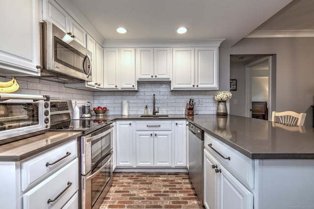 714 Popes Island Rd Unit 714, Milford, CT 06461 - kitchen featuring a sink, stainless steel appliances, a peninsula, brick flooring, and white cabinetry