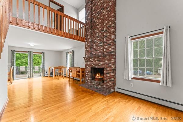 5 Conrad Ct, Ledyard, CT 06335 - unfurnished living room featuring a baseboard heating unit, wood finished floors, a high ceiling, and a fireplace