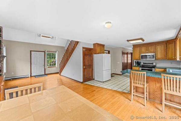 5 Conrad Ct, Ledyard, CT 06335 - kitchen with appliances with stainless steel finishes, baseboard heating, light wood finished floors, brown cabinetry, and dark countertops
