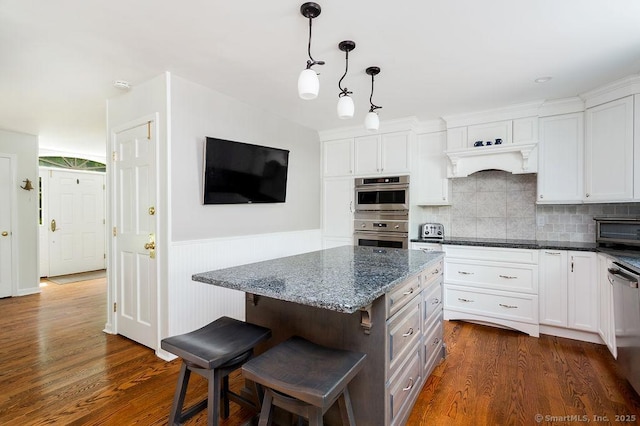 12 Fawn Ridge Dr, Brookfield, CT 06804 - kitchen featuring appliances with stainless steel finishes, white cabinets, a breakfast bar area, dark wood-style floors, and a wainscoted wall