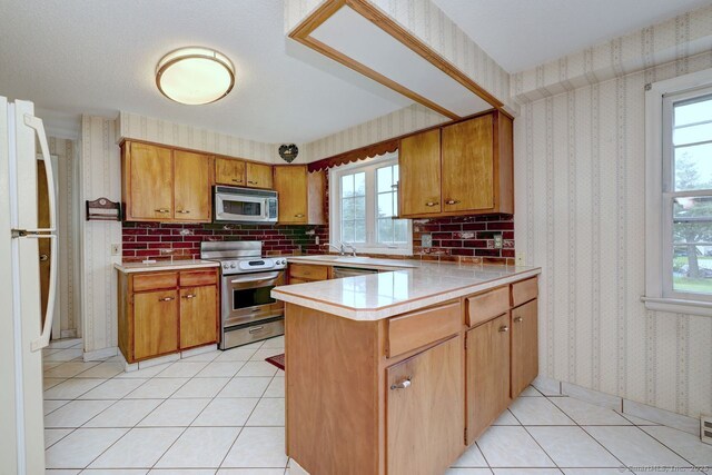 423 Baldwin Ave, Meriden, CT 06450 - kitchen featuring stainless steel appliances, a peninsula, wallpapered walls, brown cabinets, and light countertops