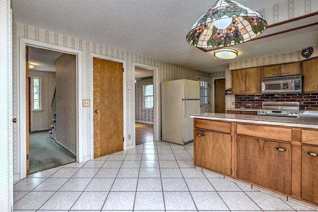 423 Baldwin Ave, Meriden, CT 06450 - kitchen with stainless steel microwave, freestanding refrigerator, wallpapered walls, range, and brown cabinets