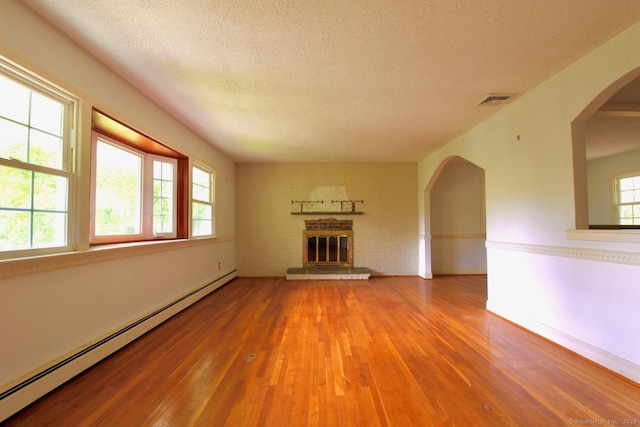 73 Devils Garden Rd, Norwalk, CT 06854 - unfurnished living room featuring baseboard heating, wood finished floors, a brick fireplace, a textured ceiling, and arched walkways