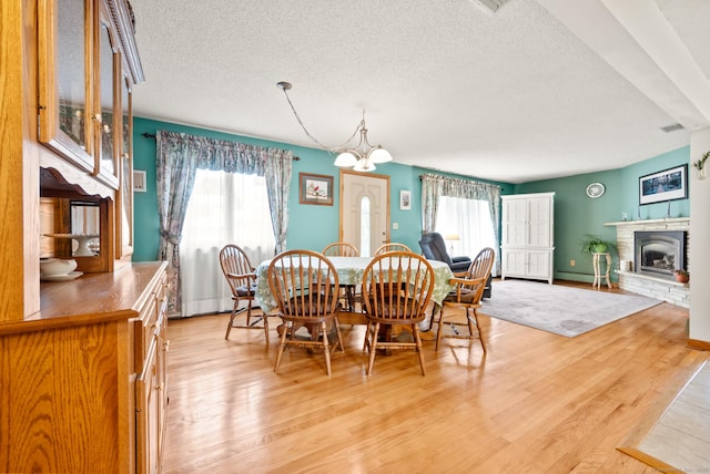 223 Beach Rd, Wolcott, CT 06716 - dining space featuring a textured ceiling, healthy amount of natural light, light wood finished floors, a chandelier, and a stone fireplace