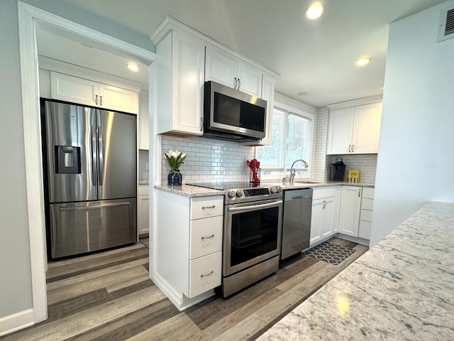 25 Milesfield Ave, Milford, CT 06460 - kitchen featuring appliances with stainless steel finishes, wood finished floors, backsplash, white cabinets, and light stone counters