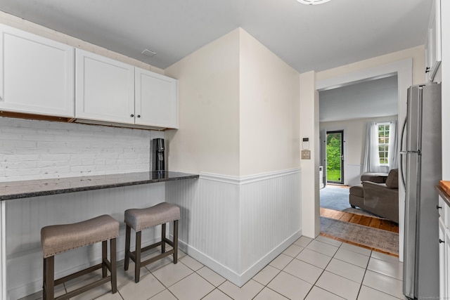 517 Wolcott Hill Rd, Wethersfield, CT 06109 - kitchen featuring freestanding refrigerator, a wainscoted wall, white cabinetry, dark stone countertops, and a kitchen bar