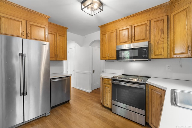 1897 Stanley St, New Britain, CT 06053 - kitchen featuring stainless steel appliances, light countertops, light wood-style flooring, arched walkways, and brown cabinetry
