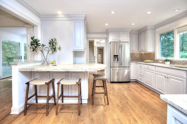 52 Woodside Ave, Westport, CT 06880 - kitchen featuring stainless steel fridge with ice dispenser, a breakfast bar, ornamental molding, white cabinetry, and light wood-type flooring