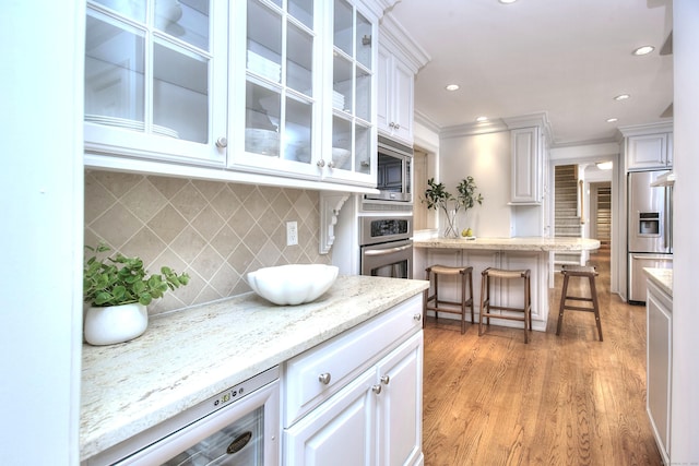 52 Woodside Ave, Westport, CT 06880 - kitchen featuring stainless steel appliances, white cabinetry, glass insert cabinets, light wood-style floors, and ornamental molding