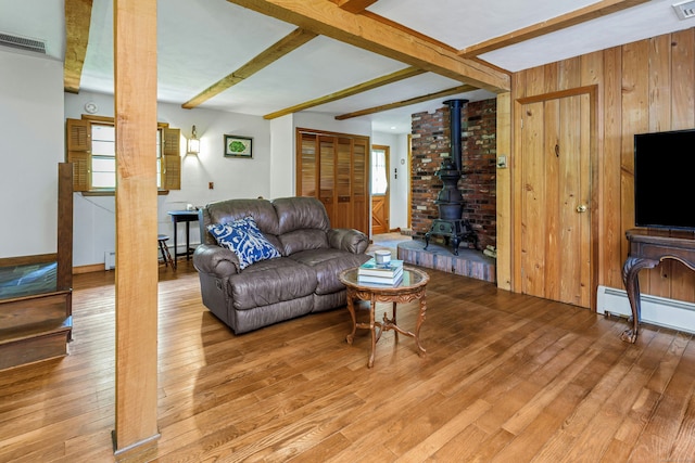 475 Hoyt St, Darien, CT 06820 - living room with a wood stove, light wood finished floors, wooden walls, beam ceiling, and a baseboard radiator