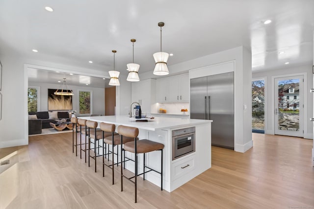 261 N St, Ridgefield, CT 06877 - kitchen featuring stainless steel built in refrigerator, a large island with sink, white cabinets, a breakfast bar area, and light wood-type flooring