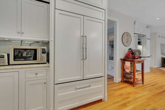2 Lake Louise Dr, Westbrook, CT 06498 - kitchen view of stainless steel microwave, light wood-style floors, white cabinetry, recessed lighting, and backsplash