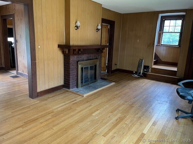 79 Van St, Stratford, CT 06614 - living area featuring light wood finished floors, a brick fireplace, wooden walls, and baseboards