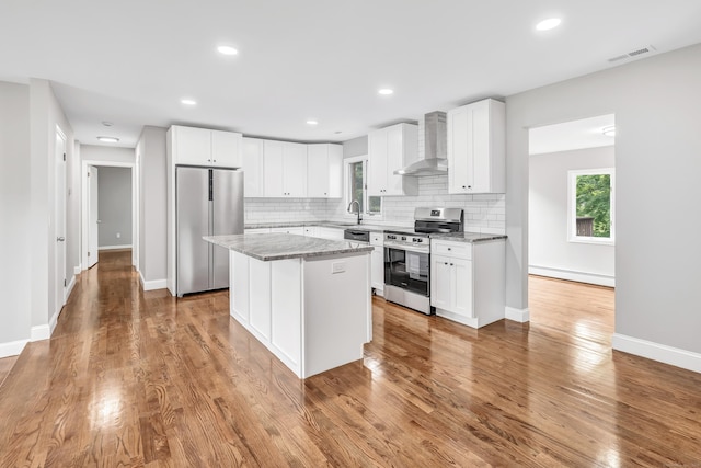 325 River Rd, Hamden, CT 06518 - kitchen featuring appliances with stainless steel finishes, wall chimney range hood, a baseboard radiator, a kitchen island, and tasteful backsplash