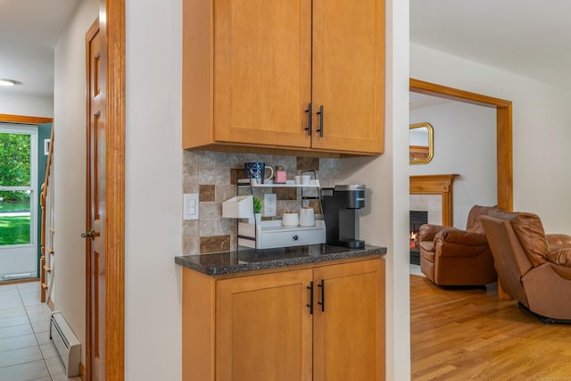 113 Charles St, Tolland, CT 06084 - kitchen featuring a baseboard radiator, decorative backsplash, light wood-style flooring, a tile fireplace, and dark stone countertops