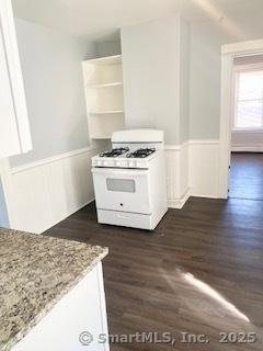 67 Ash St, Bridgeport, CT 06605 - kitchen with white gas range oven, wainscoting, dark wood finished floors, open shelves, and light stone counters