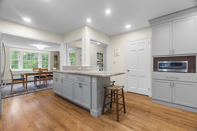 89 Pease Rd, Woodbridge, CT 06525 - kitchen featuring stainless steel microwave, a breakfast bar area, light wood finished floors, gray cabinetry, and light stone countertops